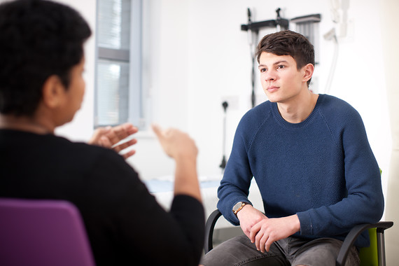 Image shows two individuals sat facing each other on chairs in conversation